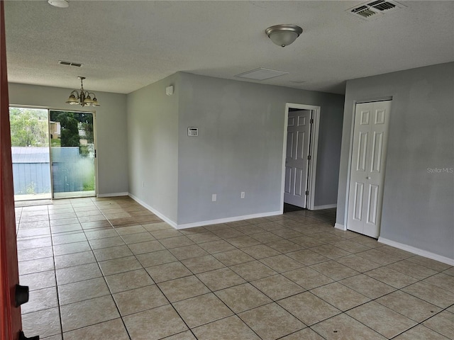 unfurnished room featuring an inviting chandelier, a textured ceiling, and light tile patterned floors