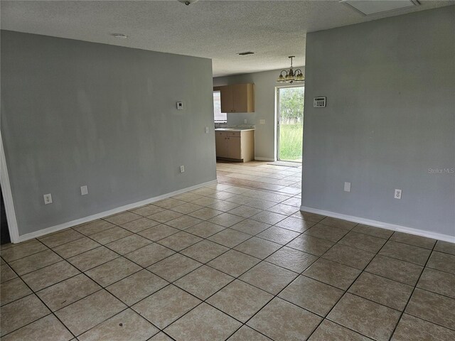 tiled spare room with a textured ceiling and a chandelier