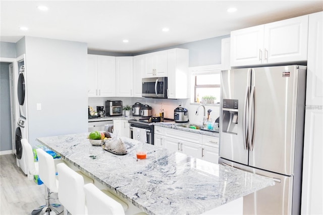 kitchen featuring stacked washer and clothes dryer, a kitchen breakfast bar, sink, appliances with stainless steel finishes, and white cabinetry