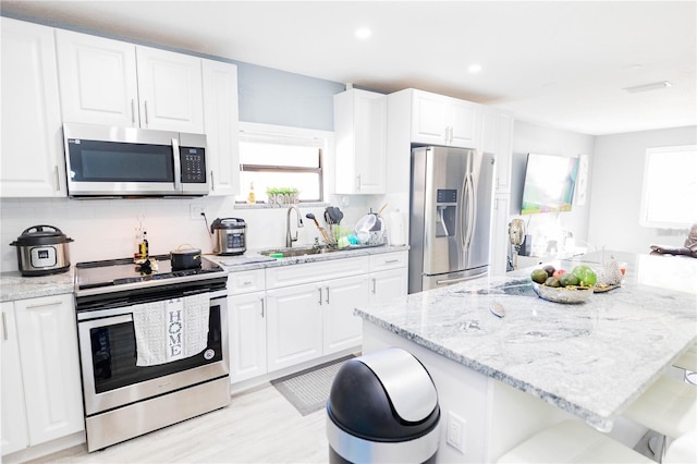 kitchen with light stone countertops, sink, a breakfast bar area, white cabinets, and appliances with stainless steel finishes