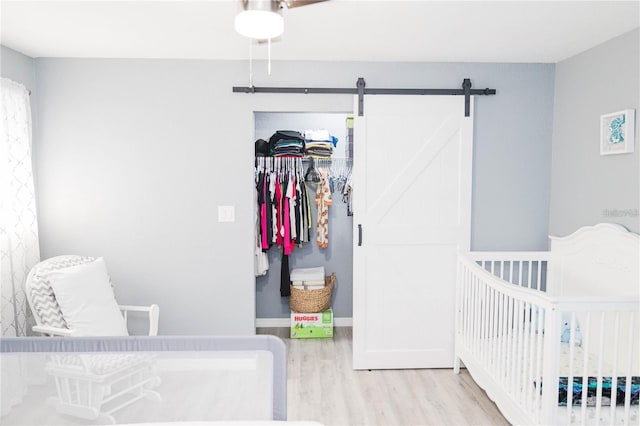 bedroom featuring a barn door, light hardwood / wood-style floors, and a nursery area