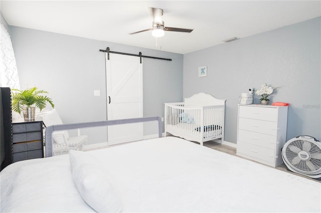 bedroom featuring ceiling fan, a barn door, and wood-type flooring