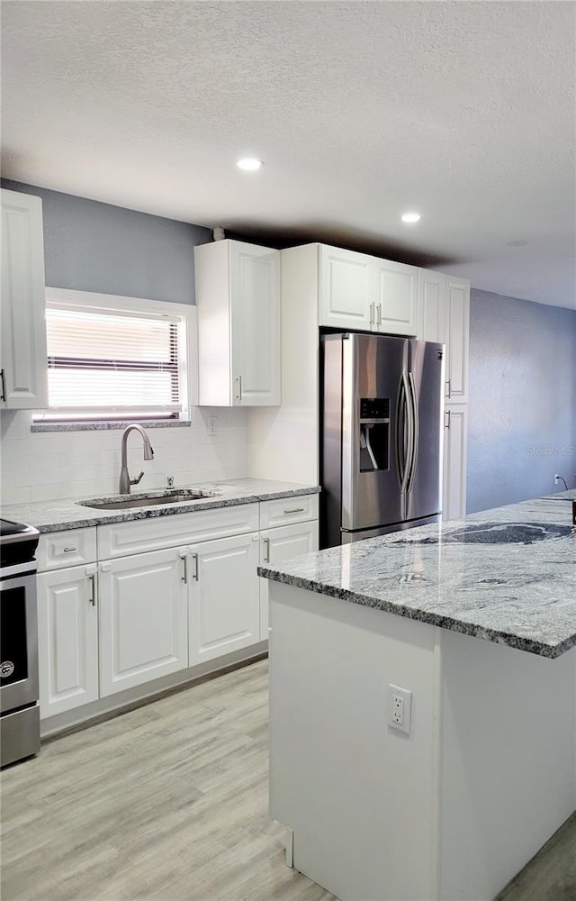 kitchen with white cabinets, sink, light hardwood / wood-style floors, light stone counters, and stainless steel appliances