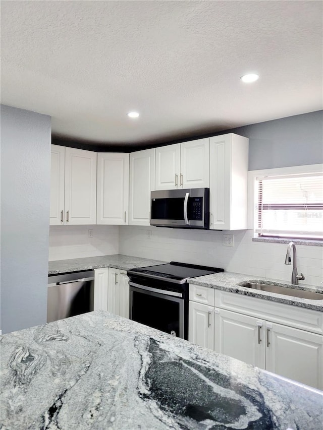 kitchen with white cabinetry, sink, stainless steel appliances, light stone counters, and a textured ceiling