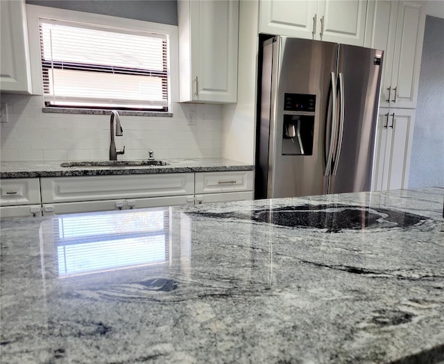 kitchen with white cabinets, light stone countertops, stainless steel fridge with ice dispenser, and sink