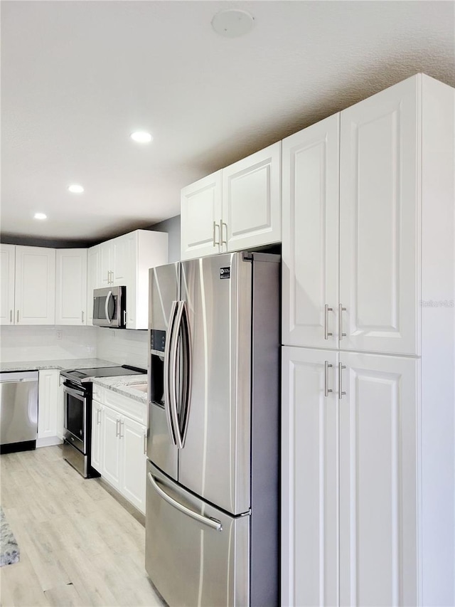 kitchen featuring white cabinetry, stainless steel appliances, light stone counters, light hardwood / wood-style floors, and decorative backsplash