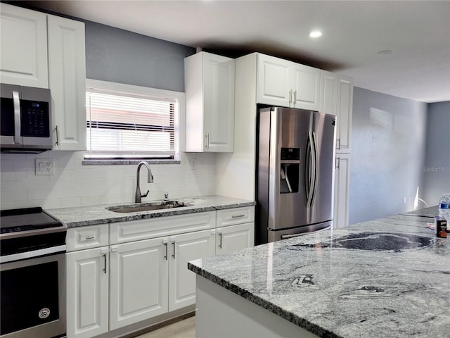 kitchen featuring light stone counters, stainless steel appliances, white cabinetry, and sink