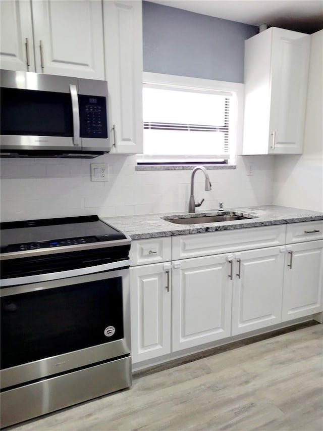 kitchen with light stone counters, sink, white cabinets, and stainless steel appliances