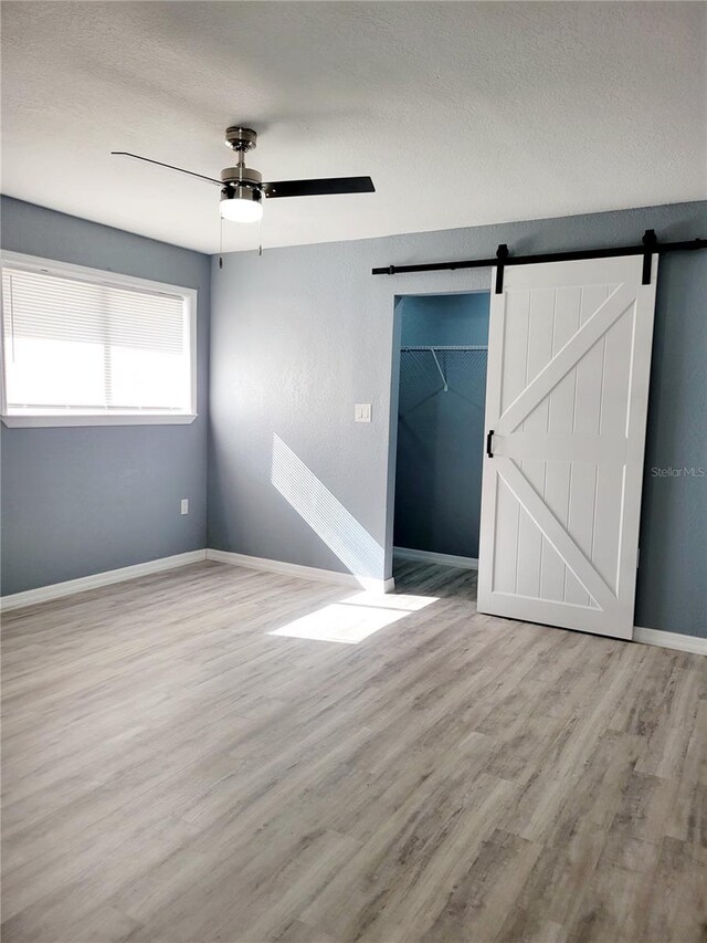 spare room featuring a barn door, ceiling fan, light hardwood / wood-style flooring, and a textured ceiling