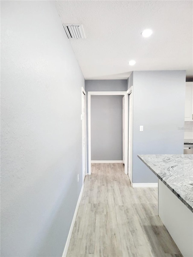 hall with a textured ceiling and light hardwood / wood-style flooring