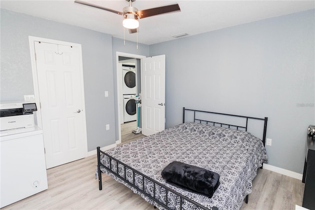 bedroom featuring ceiling fan, light hardwood / wood-style floors, and stacked washer and clothes dryer