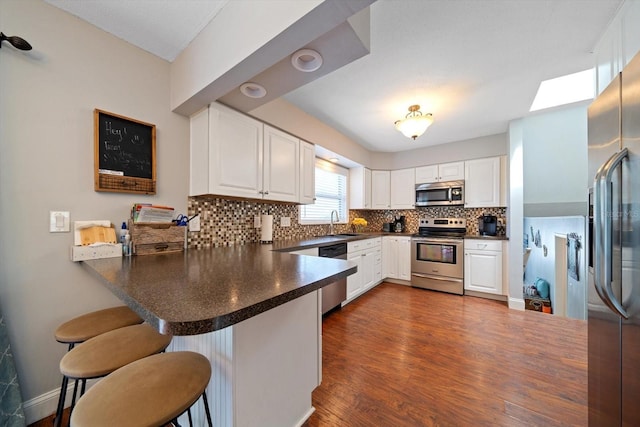 8212 Forest Cir, Seminole, FL 33776 - kitchen featuring appliances with stainless steel finishes, a peninsula, a sink, tasteful backsplash, and dark countertops