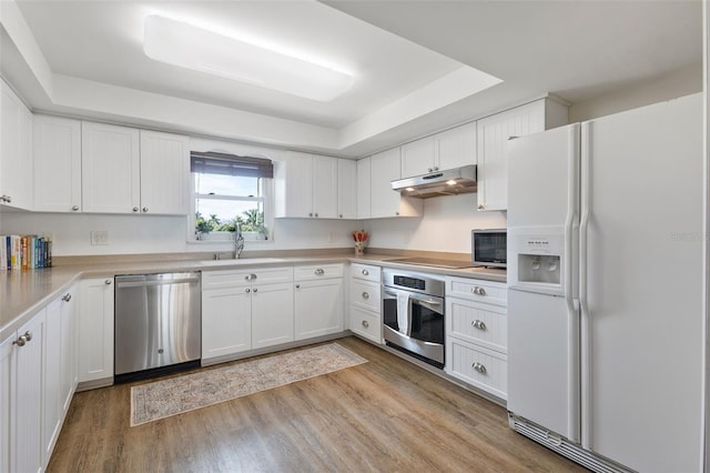 kitchen featuring white cabinets, light hardwood / wood-style flooring, appliances with stainless steel finishes, sink, and a tray ceiling