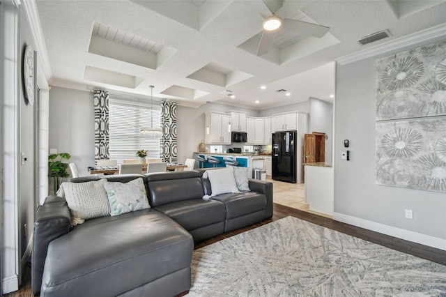 living room with ceiling fan, beam ceiling, light hardwood / wood-style flooring, coffered ceiling, and crown molding