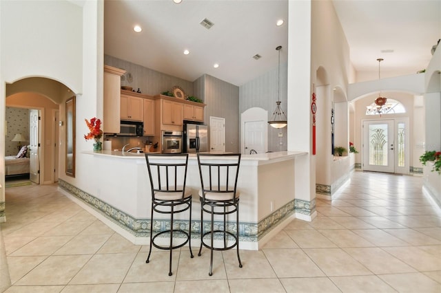 kitchen featuring decorative light fixtures, stainless steel appliances, kitchen peninsula, high vaulted ceiling, and a breakfast bar