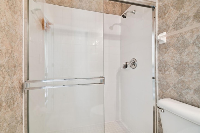 bathroom with tile walls, toilet, and a shower with shower door