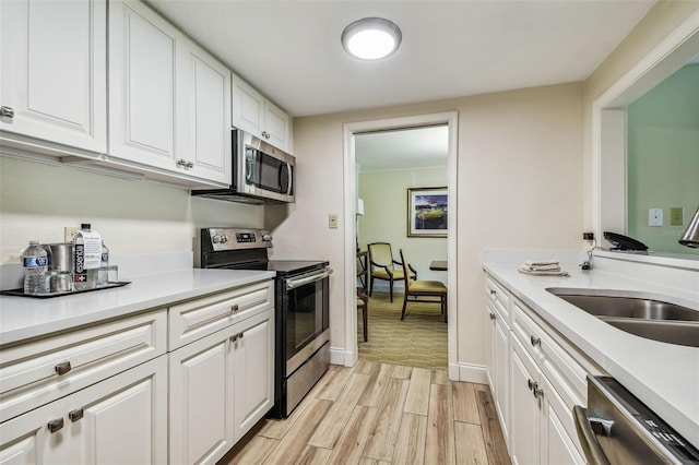 kitchen featuring appliances with stainless steel finishes, white cabinetry, sink, and light hardwood / wood-style floors