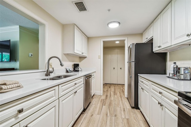 kitchen with crown molding, stainless steel appliances, sink, white cabinets, and light hardwood / wood-style floors