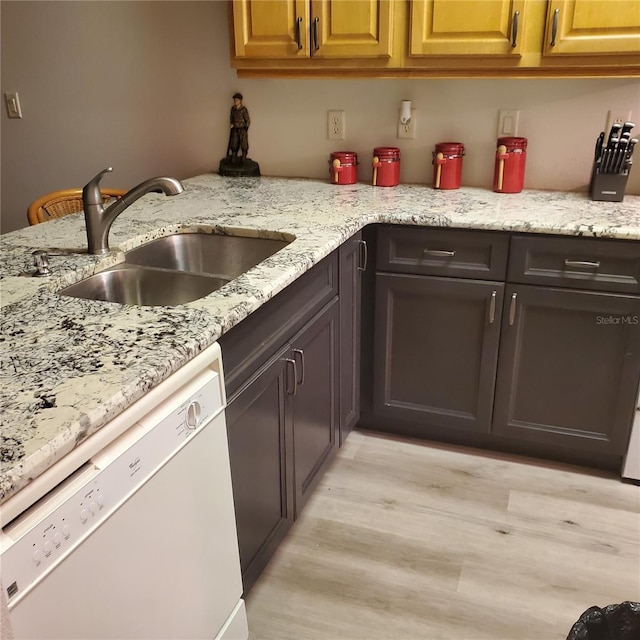 kitchen with light wood-type flooring, dark brown cabinets, white dishwasher, light stone countertops, and sink