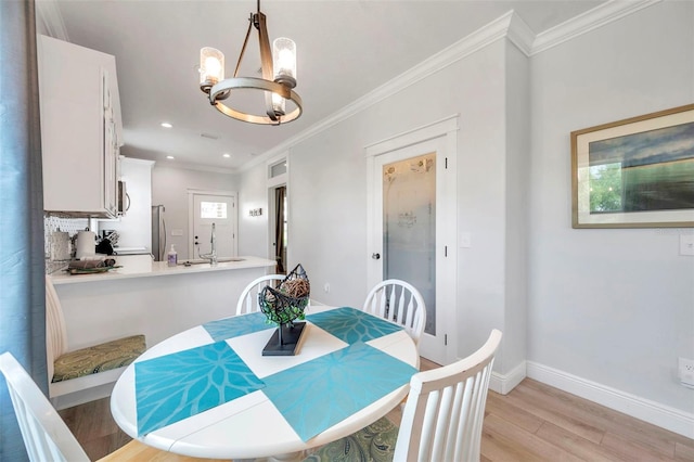 dining space with an inviting chandelier, light hardwood / wood-style flooring, sink, and ornamental molding