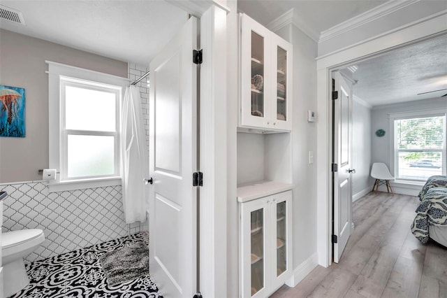 bathroom featuring tile walls, walk in shower, wood-type flooring, ornamental molding, and toilet