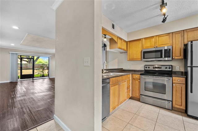 kitchen with a textured ceiling, light wood-type flooring, appliances with stainless steel finishes, sink, and ornamental molding