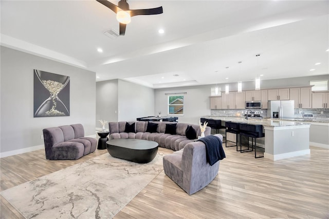 living room featuring light hardwood / wood-style flooring, a raised ceiling, and ceiling fan