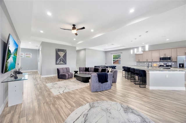 living room with a tray ceiling, ceiling fan, light hardwood / wood-style flooring, and sink