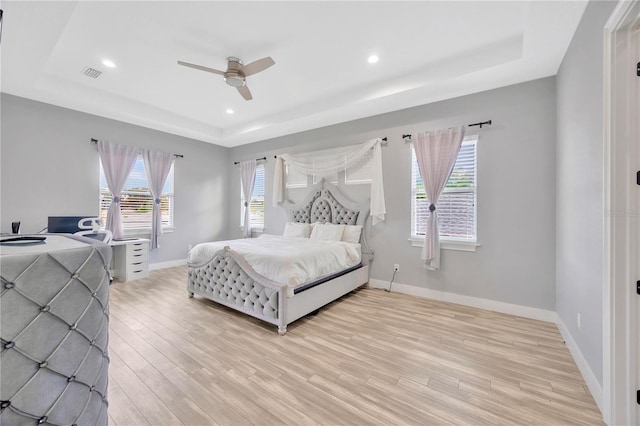 bedroom with a raised ceiling, ceiling fan, and light wood-type flooring