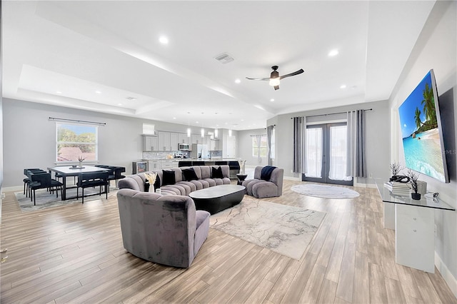 living room featuring ceiling fan, a raised ceiling, and light wood-type flooring