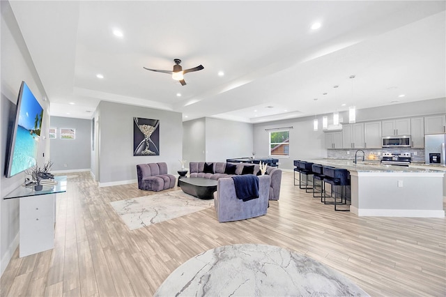 living room featuring a raised ceiling, ceiling fan, sink, and light hardwood / wood-style floors