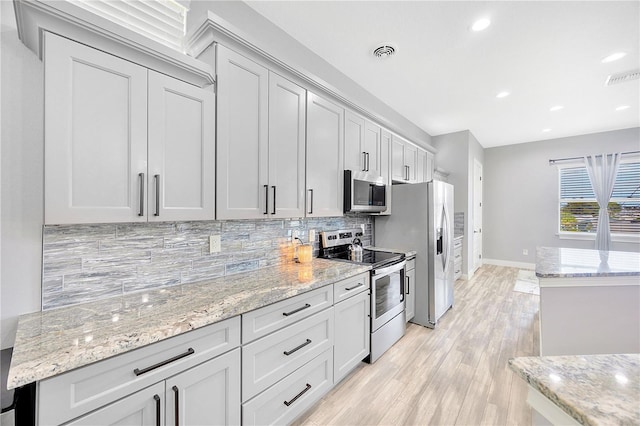 kitchen featuring light stone countertops, appliances with stainless steel finishes, backsplash, and light hardwood / wood-style flooring