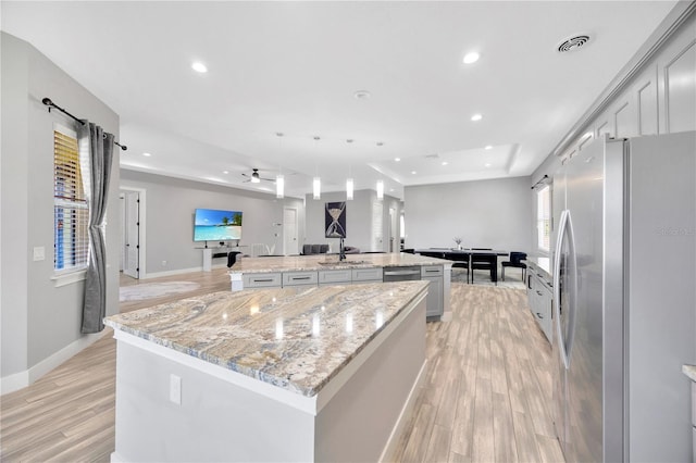 kitchen featuring light stone countertops, a large island with sink, and stainless steel refrigerator