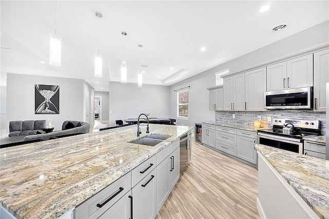 kitchen with light stone countertops, stainless steel appliances, a center island with sink, and sink