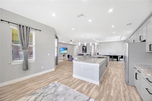 kitchen featuring ceiling fan, light stone counters, an island with sink, and light hardwood / wood-style flooring