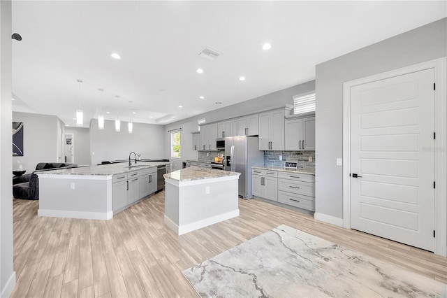 kitchen with gray cabinetry, light stone countertops, stainless steel appliances, pendant lighting, and a center island with sink