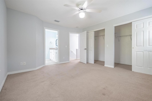 unfurnished bedroom with light colored carpet, connected bathroom, two closets, and ceiling fan