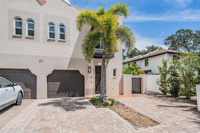 view of front of home featuring a gate, fence, an attached garage, stucco siding, and decorative driveway