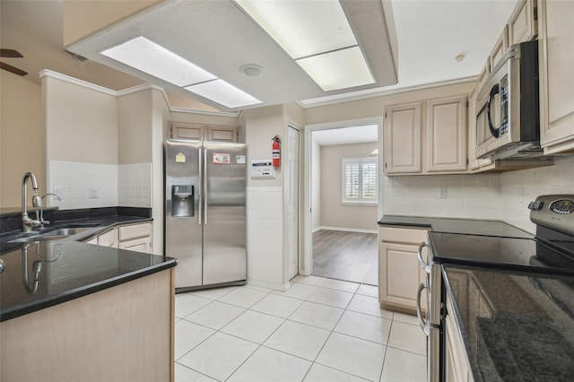 kitchen featuring dark stone countertops, ornamental molding, stainless steel appliances, sink, and light brown cabinets