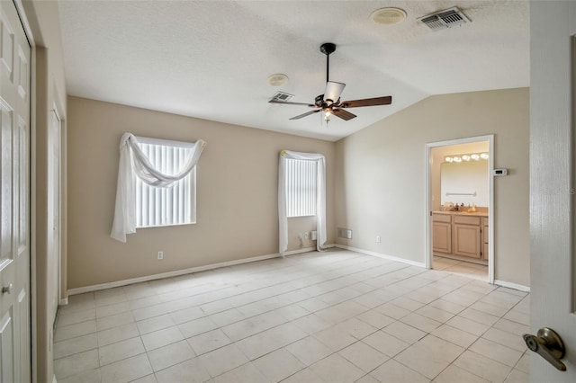 unfurnished bedroom with a textured ceiling, connected bathroom, ceiling fan, vaulted ceiling, and light tile patterned flooring