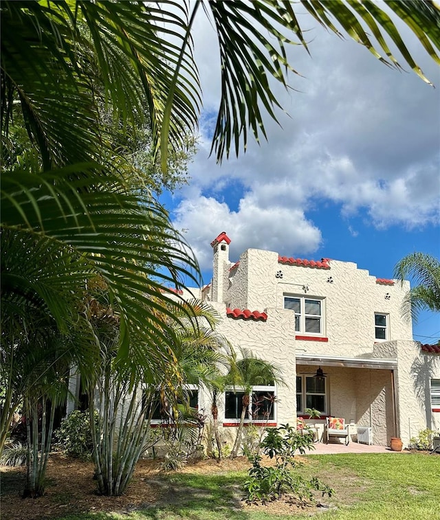 rear view of house with stucco siding, a patio area, a lawn, and a chimney