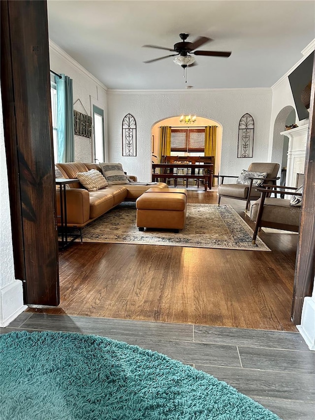 living room featuring dark wood-type flooring, ceiling fan with notable chandelier, and ornamental molding