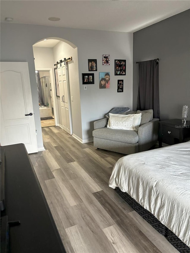 bedroom featuring ensuite bathroom, a barn door, and light hardwood / wood-style floors