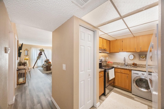 kitchen with light stone countertops, washer / clothes dryer, sink, stainless steel range with electric stovetop, and light wood-type flooring