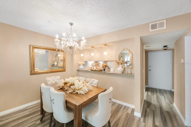 dining room with a textured ceiling, an inviting chandelier, and wood-type flooring