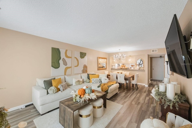 living room with light wood-type flooring, a textured ceiling, and an inviting chandelier