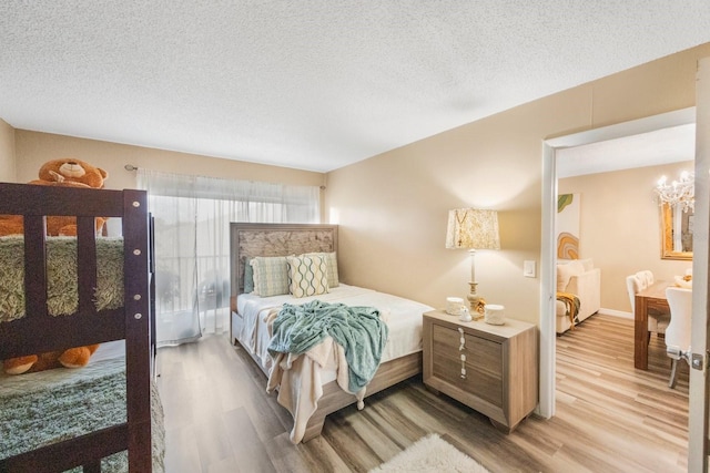 bedroom featuring a textured ceiling, light hardwood / wood-style flooring, and an inviting chandelier