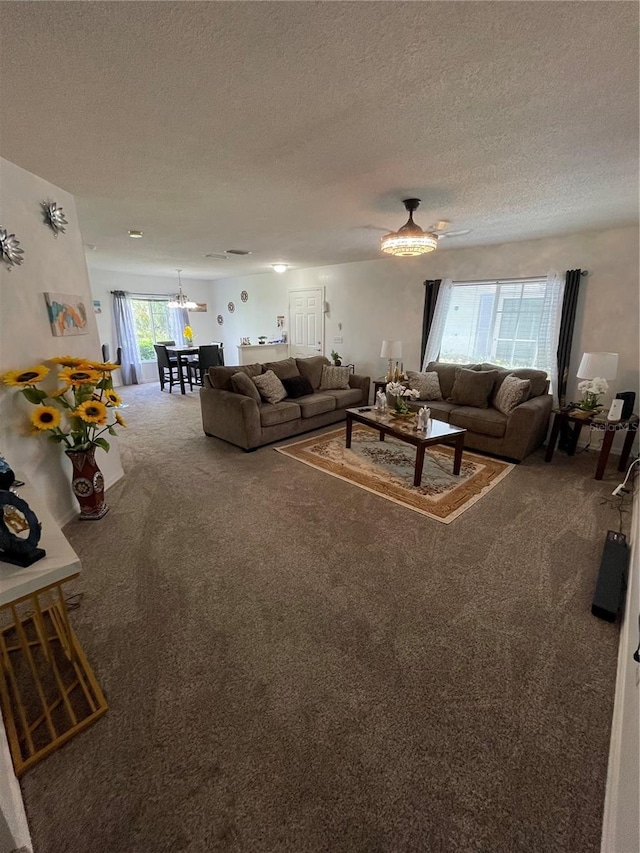 unfurnished living room featuring a textured ceiling, ceiling fan with notable chandelier, and carpet