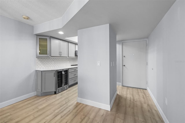 interior space featuring beverage cooler, light hardwood / wood-style floors, gray cabinets, and a textured ceiling