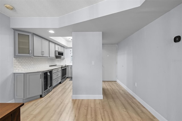 kitchen with light wood-type flooring, a textured ceiling, beverage cooler, appliances with stainless steel finishes, and gray cabinetry